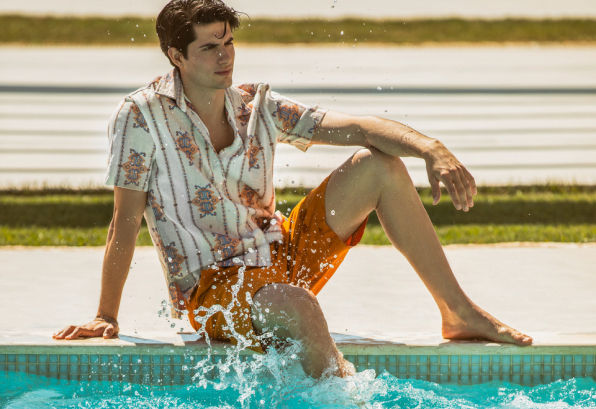 Man sitting on the edge of a pool with legs dangling in the water
