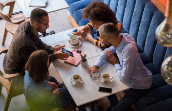 A group of peole sitting in comfy booths around a table all looking at a phone screen