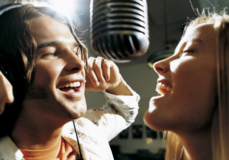 Two people singing into a recording studio microphone