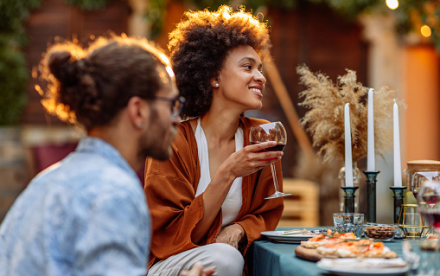 A man and a woman sit at an outdoor table enjoying a glass of wine and a bit to eat